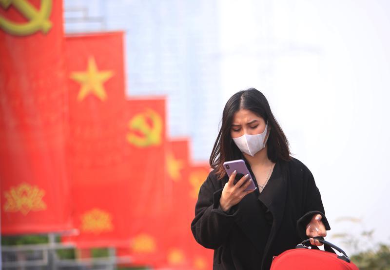 FILE - In this Jan. 23, 2021 file photo, a woman wearing face mask looks at her phone in Hanoi, Vietnam.  Vietnam says it has discovered a new coronavirus variant that’s a hybrid of strains first found in India and the U.K. The Vietnamese health minister made the announcement Saturday, May 29.   (AP Photo/Hau Dinh, File)